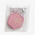 A pink hexagonal honeycomb-patterned Coaster set, with holder, sealed inside a clear plastic bag with a round white sticker that reads 'Handmade with love' and a small branded card behind it.